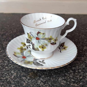 May include: White teacup and saucer with a gold rim and floral design. The teacup has the text "British Columbia Centennial 1871" printed on the inside.