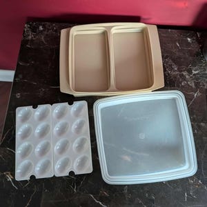 May include: A collection of vintage Tupperware containers in various shapes and sizes. Includes a divided beige tray, a clear square lid, and two white egg holders, all arranged on a dark marble surface. The containers are designed for food storage.