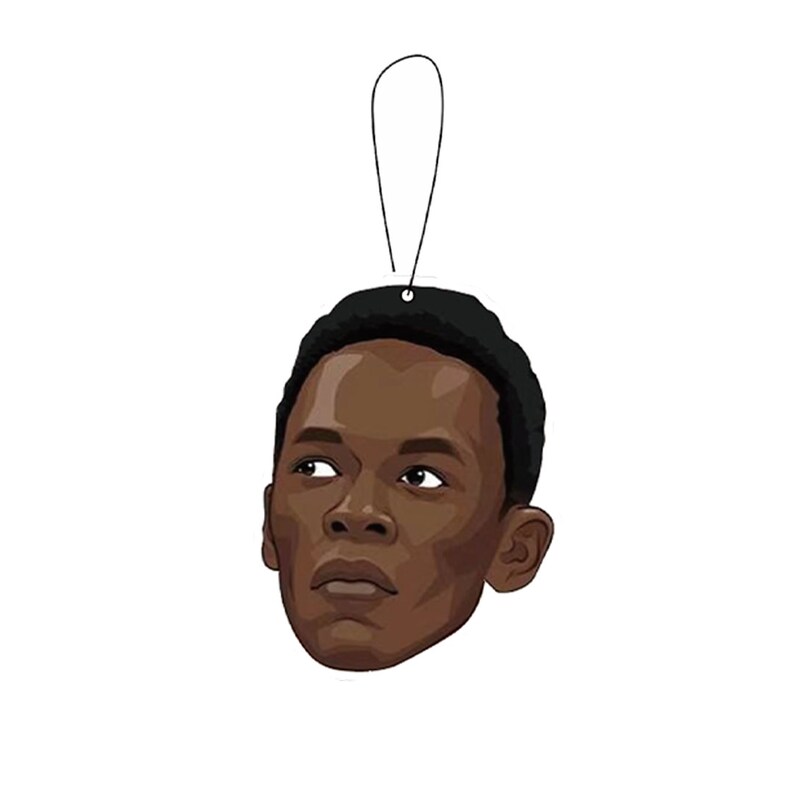 May include: A black and white cartoon illustration of a man's face with a serious expression. The image is printed on a car air freshener.