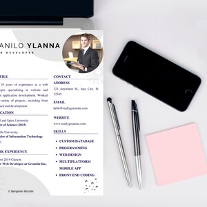 May include: A web developer's CV with the name "DANILO YLANNA" and the title "WEB DEVELOPER". The CV includes profile, education, work experience, contact information, website, and skills. A black smartphone, two pens, and a pink sticky note are also on the white surface.