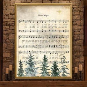 May include: A framed print of the "Silent Night" sheet music with a gold frame. The print shows musical notes, lyrics, and watercolour evergreen trees at the bottom. The text "FRAME NOT INCLUDED" is in a white circle in the upper left.