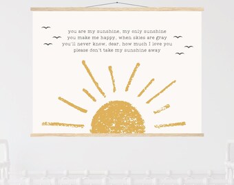 May include: A wall hanging with a yellow sun illustration and the text "you are my sunshine, my only sunshine..." in black. The artwork is displayed above a white crib, creating a nursery theme.