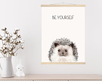 May include: A white poster with a brown wooden frame hangs on a white wall. The poster features a watercolor illustration of a hedgehog with the text "BE YOURSELF" above it.