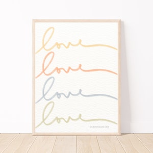 Puede incluir: Una impresión enmarcada con la palabra "love" escrita cuatro veces en diferentes colores pastel. El texto "1 Corintios 13:13" está en la parte inferior de la impresión.