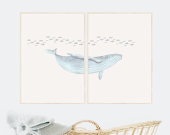 May include: A set of two framed watercolor prints featuring a blue whale swimming through a school of small fish. The whale is depicted in a light blue color, with a white background.