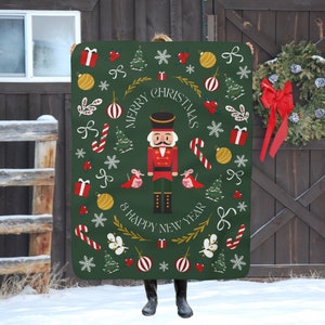 May include: Green throw blanket with a festive Christmas design featuring a Nutcracker, candy canes, ornaments, and the text "Merry Christmas & Happy New Year".