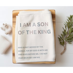 May include: A white fleece blanket with the text "I AM A SON OF THE KING" in pink, blue, and grey. The text continues with "WHO IS NOT MOVED BY THE WORLD, FOR MY GOD IS WITH ME AND GOES BEFORE ME, I DO NOT FEAR BECAUSE I AM HIS."