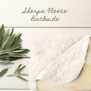May include: A close-up of the back side of a white sherpa fleece blanket. The blanket is folded in half and the soft, fluffy texture is visible.