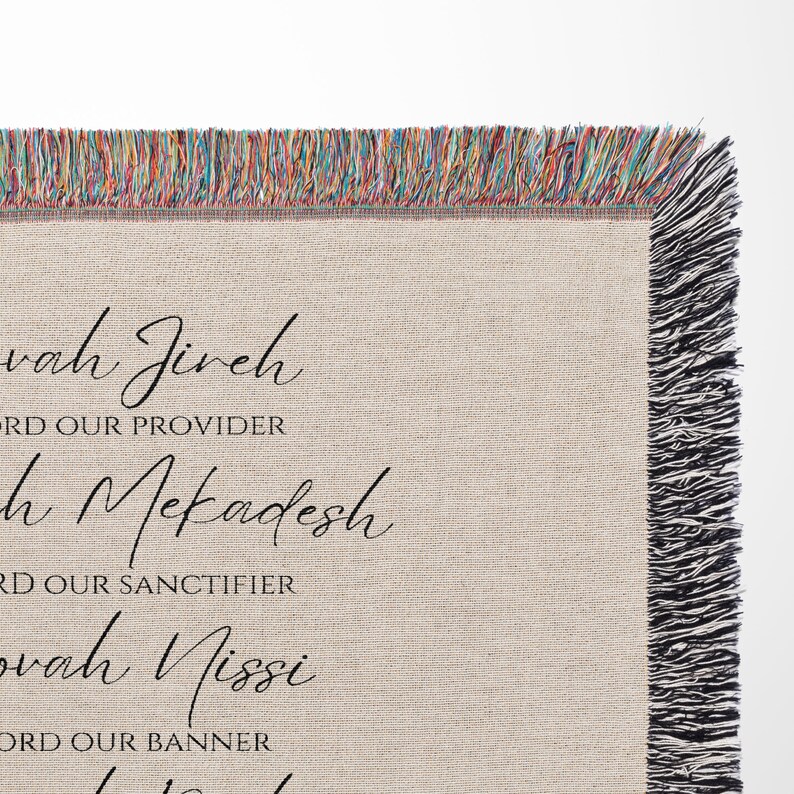 K&ouml;nnte beinhalten: Eine beige Decke mit schwarzem Schrifttext und einem Fransenrand. Der Text enth&auml;lt S&auml;tze wie "Jehovah Jireh" und "Lord Our Provider". Der Fransenrand weist eine Mischung aus Farben auf und verleiht der Decke eine dekorative Note.