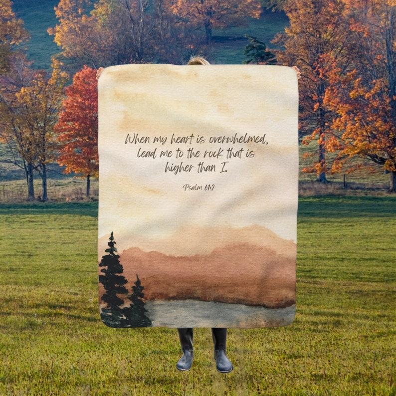 May include: A beige throw blanket with a watercolour landscape scene and the text "When my heart is overwhelmed, lead me to the rock that is higher than I. Psalm 61:2"