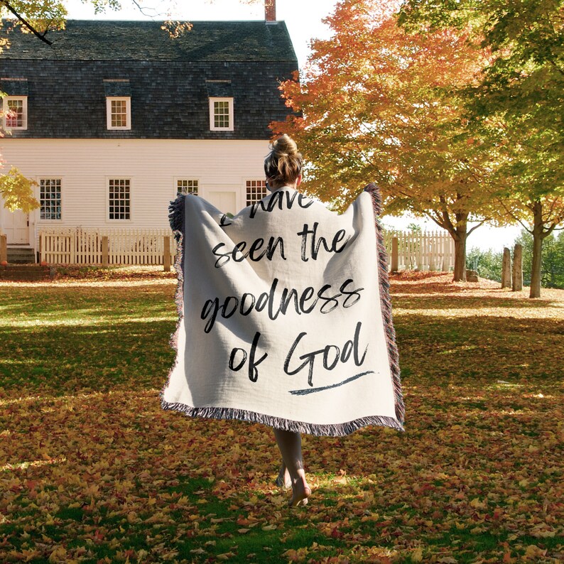 May include: A person holding a beige throw blanket with the text "I have seen the goodness of God" written in black cursive.