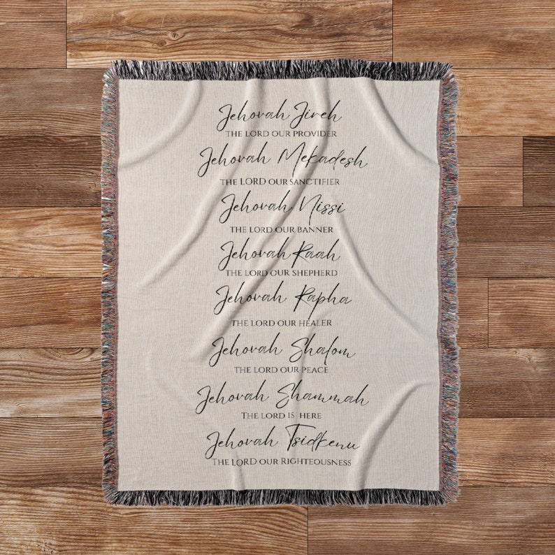 K&ouml;nnte beinhalten: Eine beige gewebte Wurfadecke mit schwarzem Text, der die Namen Gottes auflistet. Die Namen sind in einer dekorativen Schrift geschrieben. Die Decke hat einen Fransenrand und wird auf einer Holzoberfl&auml;che pr&auml;sentiert.