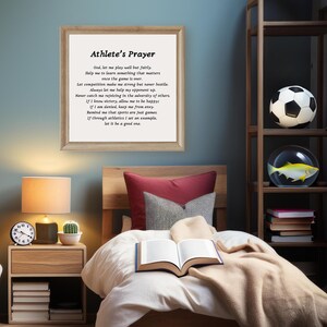 May include: A framed print with a motivational poem titled "Athlete's Prayer" about sportsmanship and perseverance. The print is hanging on a blue wall in a bedroom with a bed, a bedside table, a lamp, and a bookshelf.
