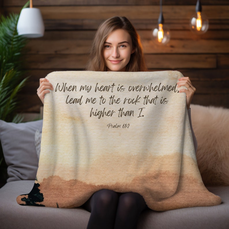 May include: A beige throw blanket with a watercolour background and the text "When my heart is overwhelmed, lead me to the rock that is higher than I. Psalm 61:2" printed in brown.
