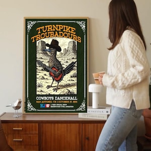 May include: A framed poster with a green background displays the text "TURNPIKE TROUBADOURS" and a roadrunner playing a guitar. The poster also includes the text "COWBOYS DANCEHALL SAN ANTONIO, TX | OCTOBER 27, 2025".