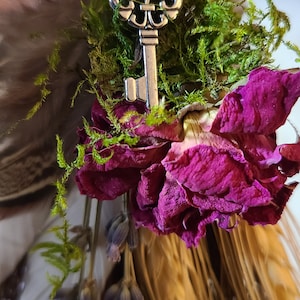 May include: A small broom with a wooden handle wrapped in twine and decorated with dried flowers, moss, and a silver key charm.