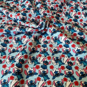 May include: Blue and white fabric with a repeating pattern of Stitch from Lilo & Stitch. The background is light blue with red flowers.