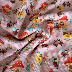 May include: Pink fabric with a repeating pattern of red and white mushroom houses, ladybugs, bees, and flowers. The ladybugs have red shells with black spots. The bees are yellow and black. The flowers are yellow, orange, and blue.