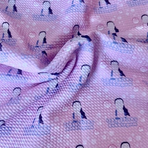 Puede incluir: Tela rosa con un patrón repetido de dos mujeres con cabello negro largo de pie en una bañera con burbujas. La tela tiene una textura de tejido de waffle.