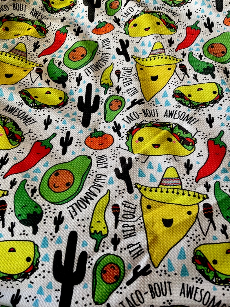 May include: A white fabric with a repeating pattern of cartoon tacos, avocados, chili peppers, and cacti. The tacos are wearing sombreros and have the text "Taco-Bout Awesome!" and "Hip Hip Cole!" The avocados have the text "Holy Guacamole!" The chili peppers are red and green. The cacti are black and green.