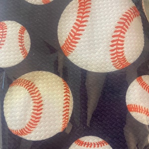 May include: A black fabric with a repeating pattern of white baseballs with red stitching.