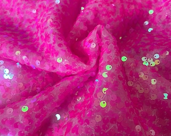 May include: Pink iridescent sequins on a sheer mesh fabric. The sequins are round and have a holographic finish.