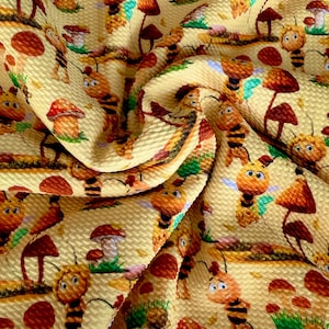 May include: Yellow fabric with a repeating pattern of cartoon bees and mushrooms. The bees are orange and black, and the mushrooms are brown and red. The fabric has a textured surface.