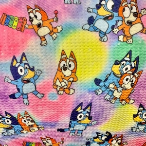 Puede incluir: Tela estampada con personajes de perros de dibujos animados azules y naranjas, sobre un fondo teñido anudado. Los perros están en varias poses, algunos sosteniendo instrumentos musicales. El fondo presenta colores rosa, amarillo y morado.