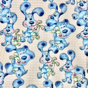 May include: A white fabric with a repeating pattern of blue cartoon dogs holding a green and yellow toy. The dogs have a light blue and white spotted pattern.
