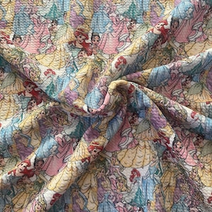 May include: A fabric with a repeating pattern of cartoon princesses in various gowns. The princesses are depicted in a variety of colors, including yellow, pink, blue, and purple. The fabric has a textured appearance.