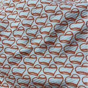 May include: White fabric with a repeating pattern of orange baseball-themed hearts.