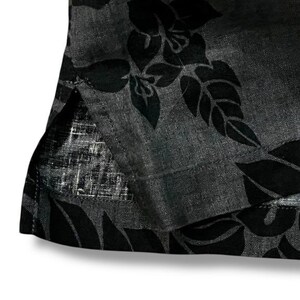 Puede incluir: Primer plano de una tela gris oscuro con un estampado floral negro. La tela parece ser un material ligero, posiblemente lino o una mezcla similar. El dise&ntilde;o floral es un patr&oacute;n repetido de hojas y flores.