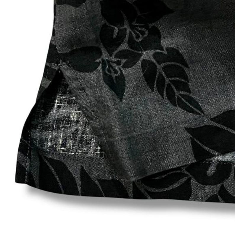 Puede incluir: Primer plano de una tela gris oscuro con un estampado floral negro. La tela parece ser un material ligero, posiblemente lino o una mezcla similar. El dise&ntilde;o floral es un patr&oacute;n repetido de hojas y flores.