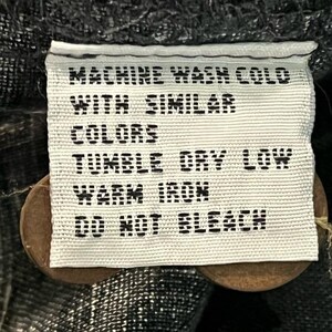 Puede incluir: Una etiqueta de tela blanca con texto negro, que incluye instrucciones de cuidado: "MACHINE WASH COLD WITH SIMILAR COLORS, TUMBLE DRY LOW, WARM IRON, DO NOT BLEACH." La etiqueta est&aacute; sujeta a una prenda con dos botones marrones.