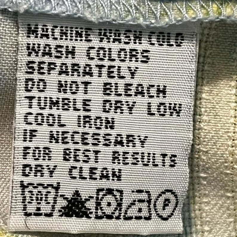 May include: A close-up of a white fabric tag with black text. The tag includes washing instructions: machine wash cold, wash colors separately, do not bleach, tumble dry low, cool iron if necessary, and dry clean.