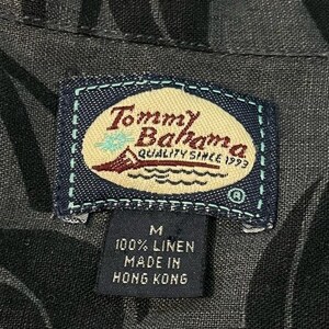 Puede incluir: Primer plano de una camisa gris oscuro con un estampado floral. La etiqueta Tommy Bahama es visible, con el nombre de la marca, un velero y el texto "QUALITY SINCE 1993". La etiqueta indica que la camisa es 100% lino y est&aacute; hecha en Hong Kong.
