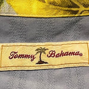 May include: Close-up of a blue patterned shirt with a yellow collar. The shirt features a label with the text "Tommy Bahama" in burgundy script, along with a palm tree graphic.