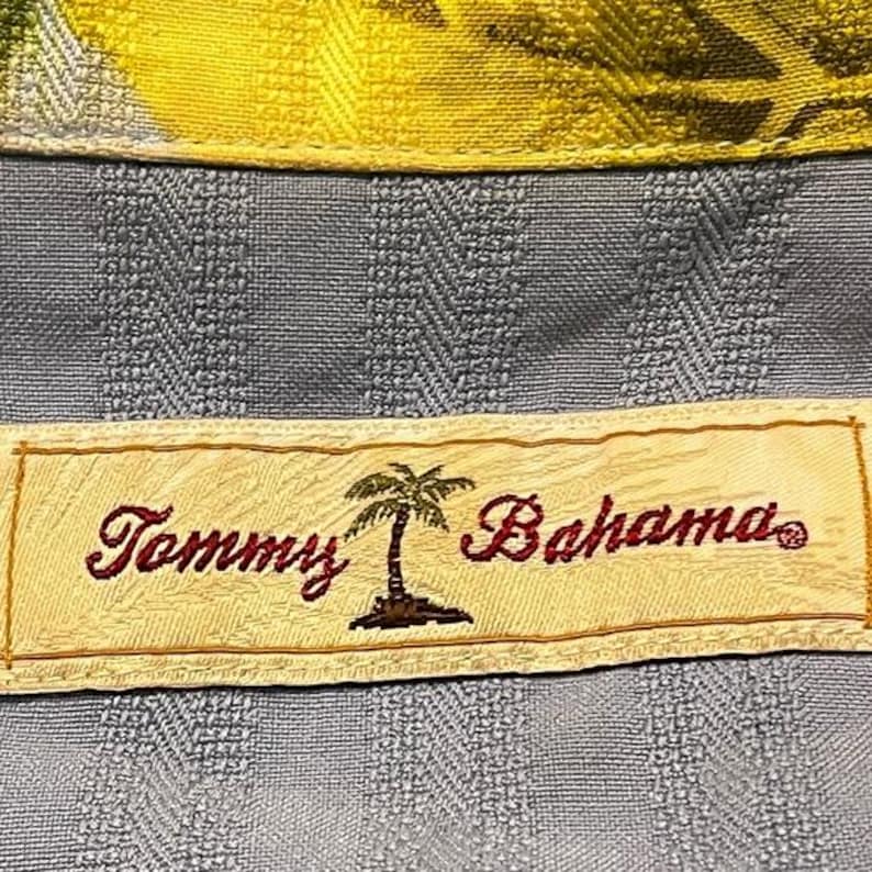 May include: Close-up of a blue patterned shirt with a yellow collar. The shirt features a label with the text "Tommy Bahama" in burgundy script, along with a palm tree graphic.