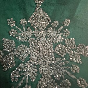 May include: Close-up of a green fabric with silver sequins and embroidery in a floral pattern.
