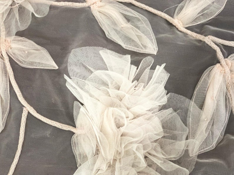 Puede incluir: Primer plano de una delicada tela de tul de color rosa claro con un dise&ntilde;o floral. La tela est&aacute; hecha de capas de tul que se juntan y se cosen para crear un efecto tridimensional.