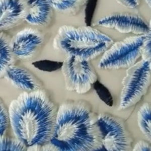 Peut inclure: Gros plan sur un tissu blanc avec des fleurs brodées bleues. Les fleurs ont un contour blanc et un centre bleu.