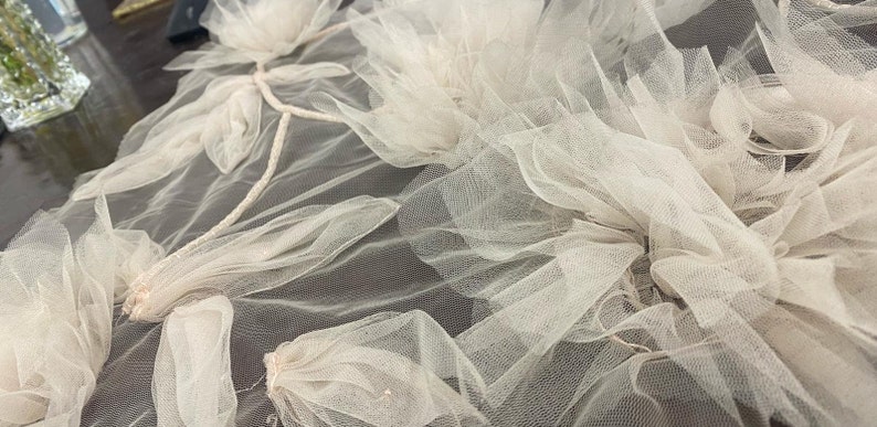 Puede incluir: Primer plano de una delicada tela de tul de color blanco roto con un dise&ntilde;o floral. La tela est&aacute; en capas y fruncida, creando un aspecto suave y rom&aacute;ntico.