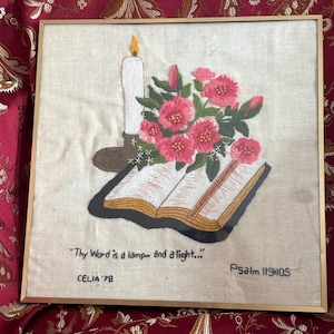 May include: Embroidered artwork in a gold frame. The image features a lit candle, a bouquet of pink flowers, and an open book. The text reads "Thy Word is a lamp and a light..." and "Psalm 119:105". Signed "CELIA '78".
