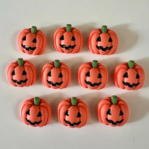 May include: Ten orange pumpkin-shaped decorations with black carved faces and green stems. These Halloween-themed embellishments are arranged in a grid pattern, perfect for seasonal crafts and decor.