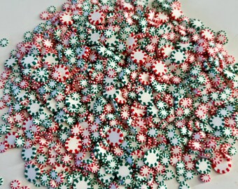 May include: A pile of small, round candies in red, white, and green. The candies have a peppermint design, with alternating colors around the edges. The candies are scattered, creating a festive and colorful display.