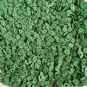 May include: A pile of small, green, rectangular polymer clay pieces, each resembling a dollar bill. The bills have black details and the number 10 printed on them. The overall effect is a textured, money-themed design.