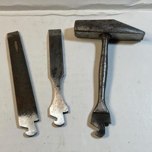 Puede incluir: Tres herramientas metálicas antiguas: una lima, un cincel y un martillo. La lima tiene una superficie texturizada, el cincel tiene una hoja plana y el martillo tiene una garra. Todas las herramientas muestran signos de desgaste.