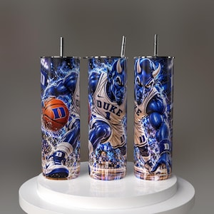 Peut inclure: Trois gobelets cylindriques avec pailles en métal, chacun arborant un graphisme de joueur de basket diable bleu en maillot blanc avec le texte DUKE et le numéro 1, sur un fond d'énergie bleue dynamique avec un ballon de basket.