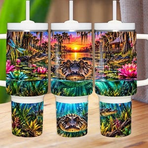 Pode incluir: Um copo de aço inoxidável branco com alça e canudo, apresentando uma cena vibrante de pântano com jacarés, nenúfares rosas e azuis, uma libélula e um pôr do sol sobre um bayou com musgo espanhol pendurado nas árvores ao fundo.