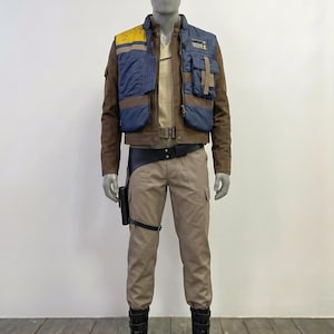 Può includere: Un set di costume composto da una giacca marrone a maniche lunghe con un gilet blu e giallo, una camicia beige e pantaloni cargo beige. L'outfit include una cintura utilitaria nera con fondina, un cinturino per la gamba e stivali neri con fibbie.